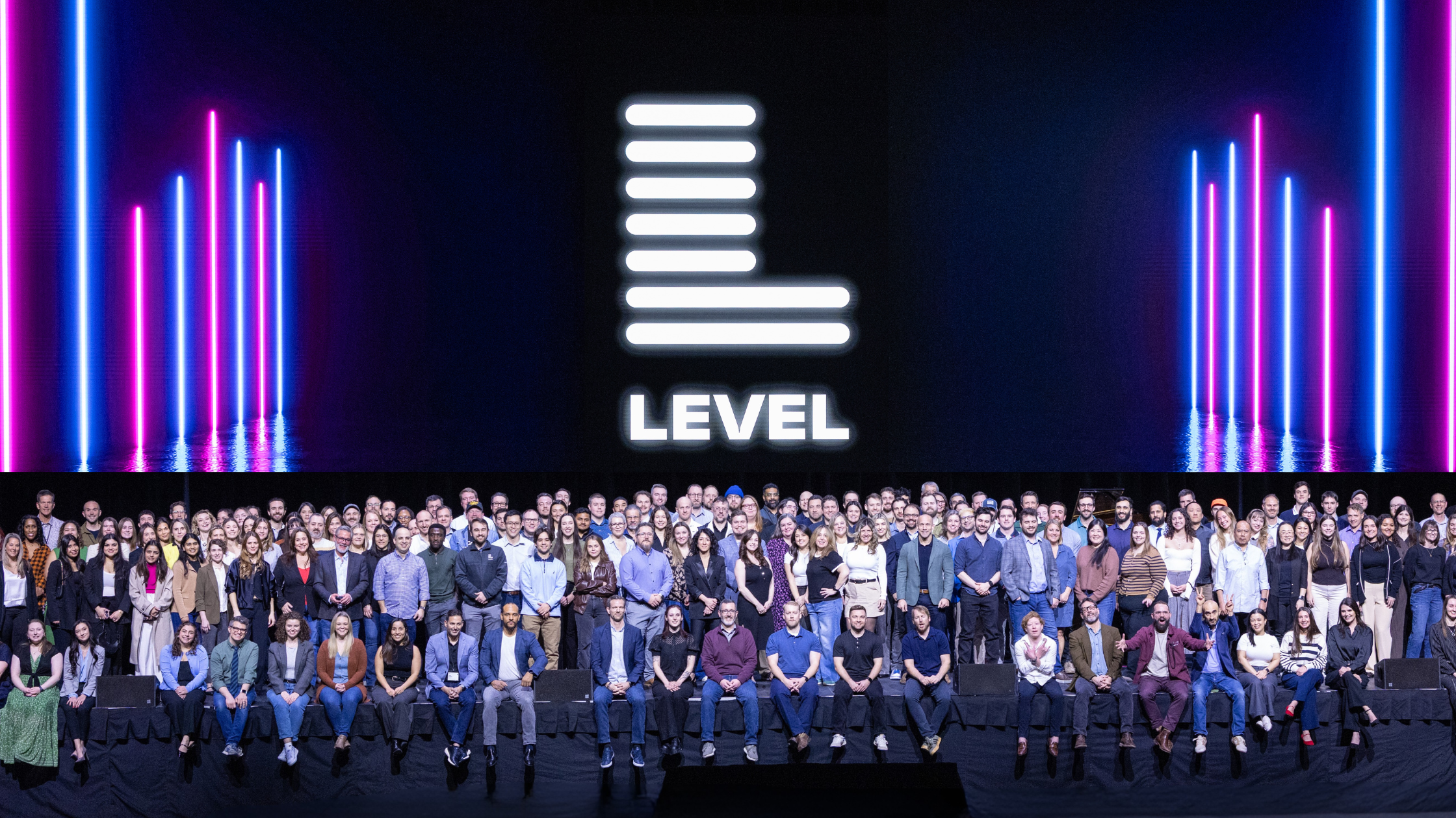 The full Level Agency team seated and standing on a stage beneath a glowing white Level logo, framed by vertical pink and blue neon lights